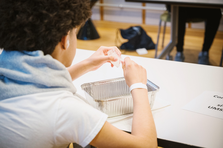 A close-up of a student modeling thermoplastic — a translucent, waxy substance — over an aluminum container that holds hot water.