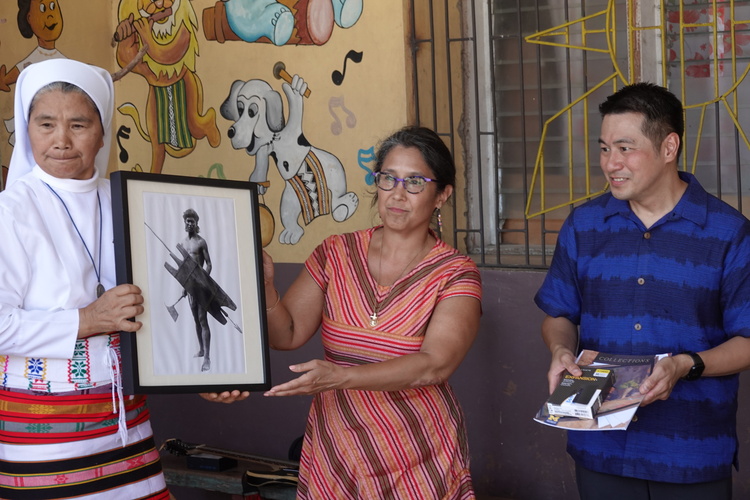 Three people exchanging a framed item