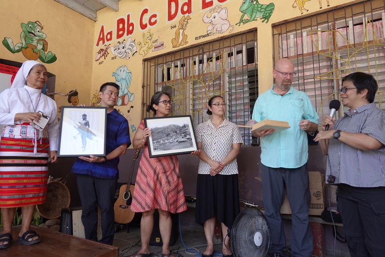 People stand in a line holding framed images during a presentation