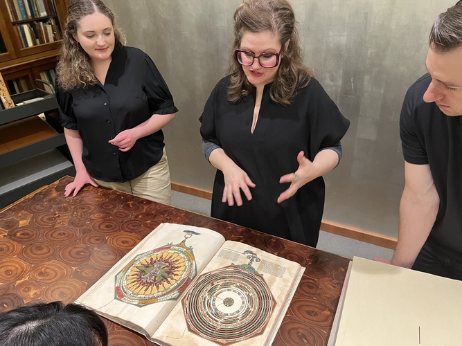 A photo of three people viewing an ancient-looking book. 
