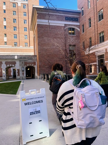A student wearing a backpack walks toward a sign that reads "University of Michigan welcomes Ann Arbor Data Dive"