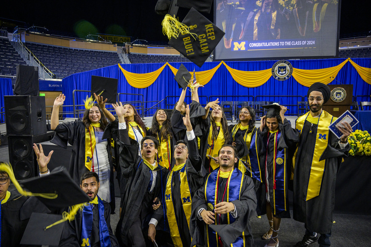 A photo of a group of UMSI graduates cheering in caps and gowns, tossing a cap in the air that reads "Keep calm and go blue"