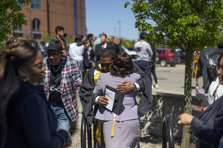 A UMSI graduate embraces a loved one, holding their graduation cap in one hand.