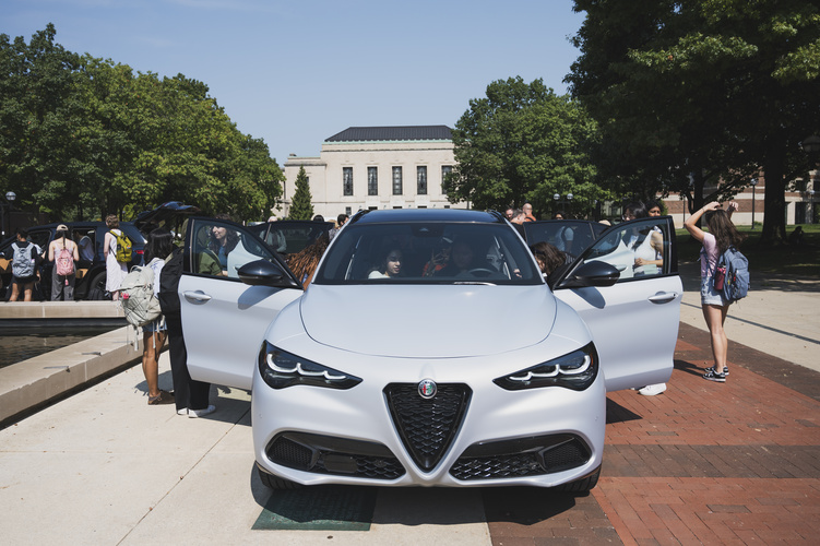 A front view of a vehicle with both doors open as students gather around and sit inside
