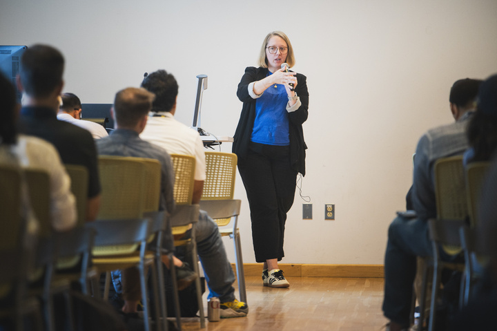 Assistant professor Rebecca Frank stands in front of an audience holding a mic.