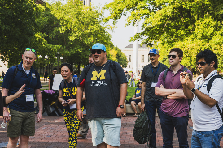 Six students gather on the U-M Diag, listening to a tour guide who is out of view.