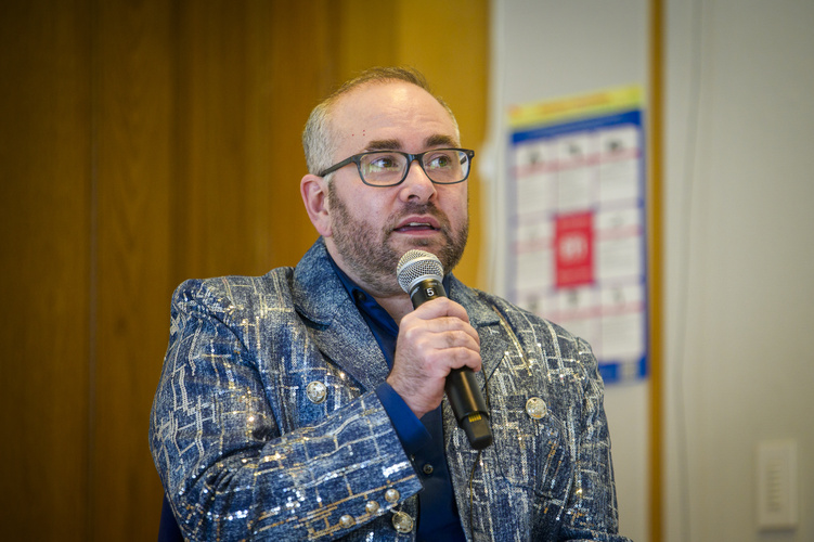 Oliver Haimson wearing a blue blazer and glasses and holding a microphone at his book launch. 