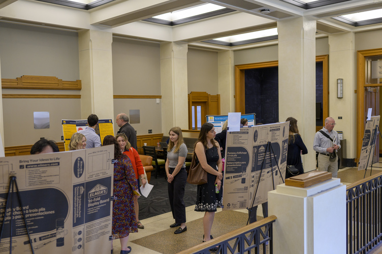 Individuals scattered throughout a long room look at display posters on easels
