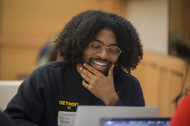 A student holds a hand to their chin thoughtfully while looking down at a laptop