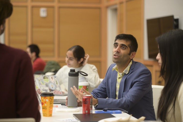Neil Tambe gestures while speaking to a group of students at a table