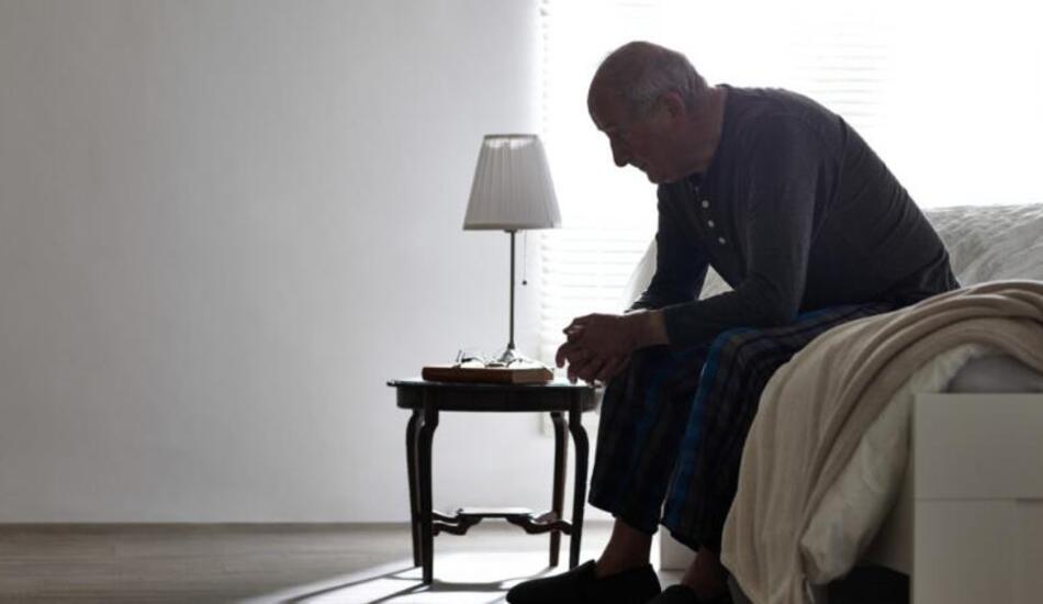 Elderly man sitting on edge of bed