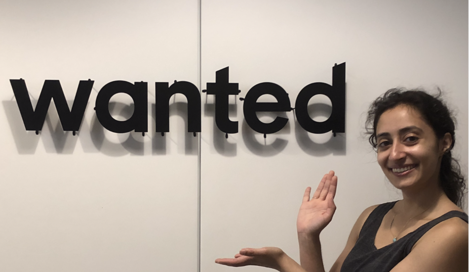 Salma Siddiqui posing next to a sign displaying the "wanted" logo.