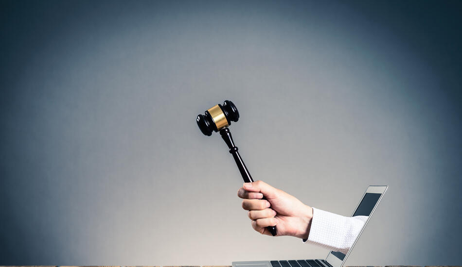 A hand holding a gavel coming out of a laptop screen