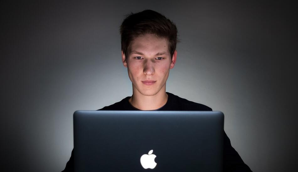 A man using a laptop, lit by the glow of the screen