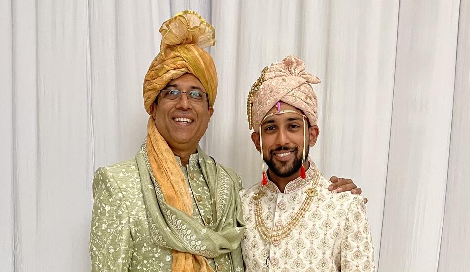 Father and son Nick and Ani Madurkar stand side by side wearing traditional Indian wedding clothing.