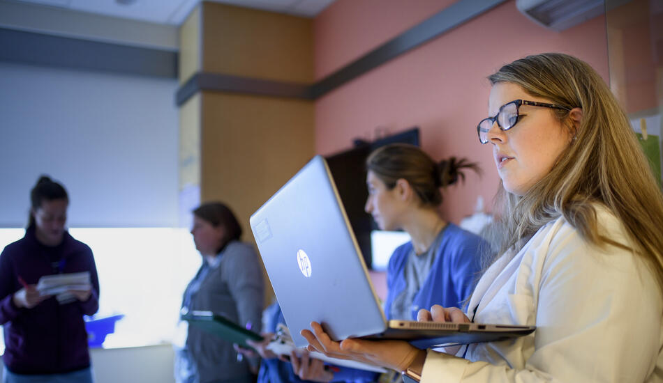 MHI student Emily Trumpower wearing a white lab coat and looking at a laptop.