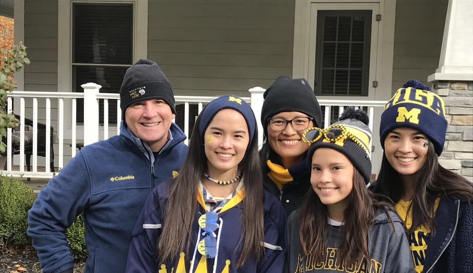 Mike and Lisa Burke with their three daughters dressed in University of Michigan apparel, standing outside. 