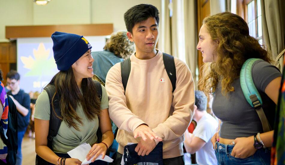 Three students talk in a large conference room.