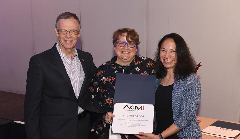 Tiffany Veinot is flanked by the past and present presidents of ACMI. They are smiling and holding an award.