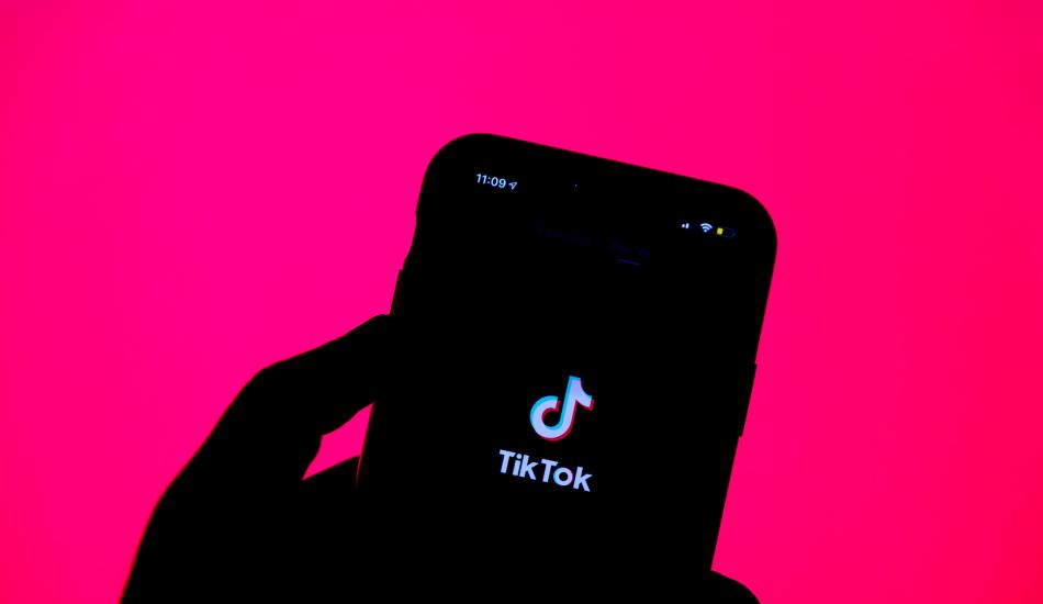 A hand holds a cell phone with the TikTok logo displayed. 