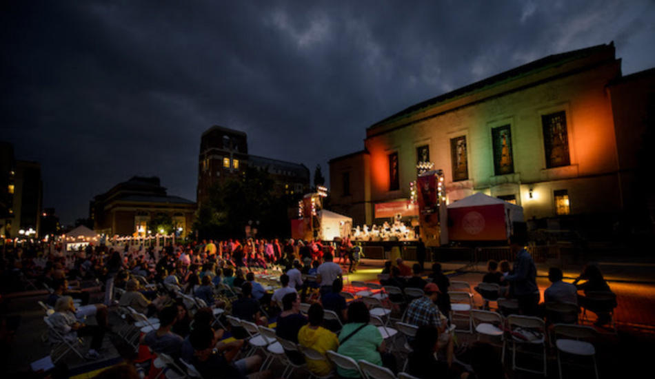 A large crowd of people sits in front of an outdoor musical performance at night at Top of the Park. 