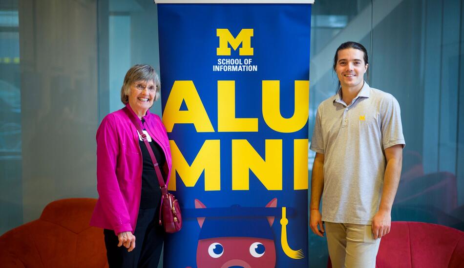 Two people stand next to a banner that says alumni