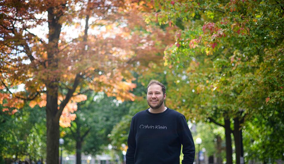 A photo of Joey Quick standing on campus with fall foliage behind him.