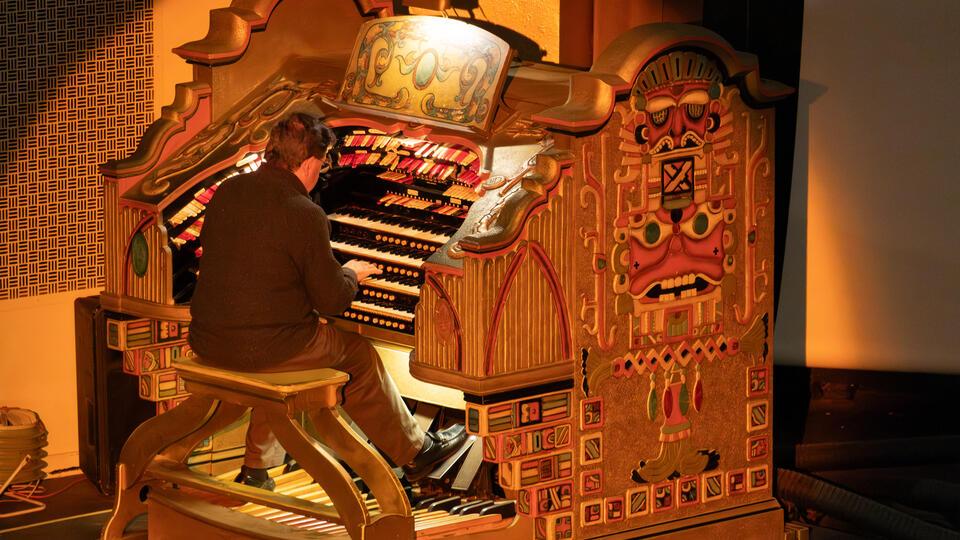 A photo of an organist performing on a Wurlitzer pipe organ. 