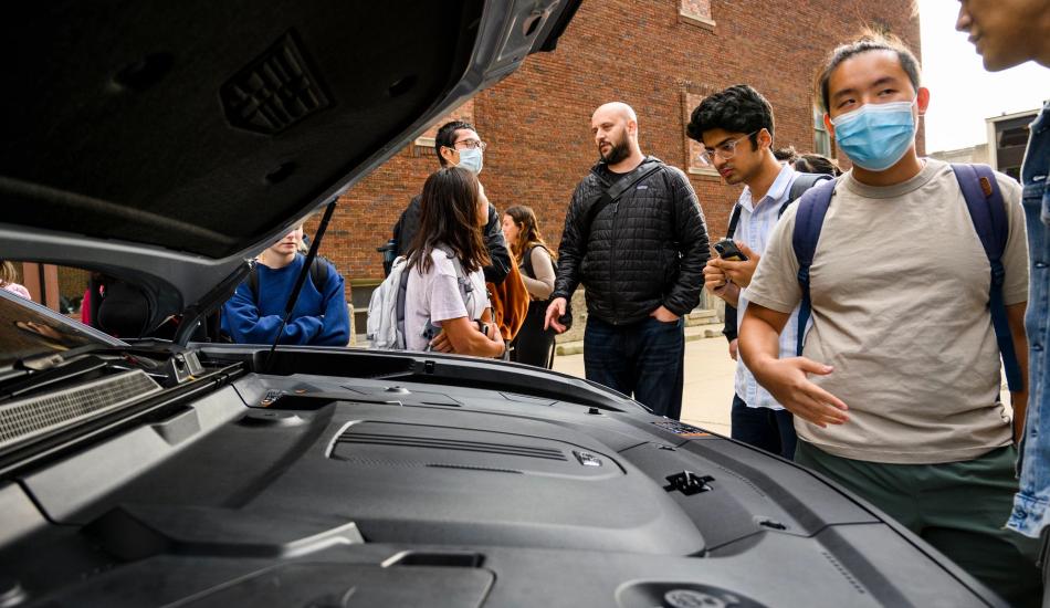 Students stand around an electric SUV with the hood open