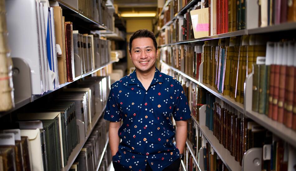 Ricky stands in an archive surrounded by books