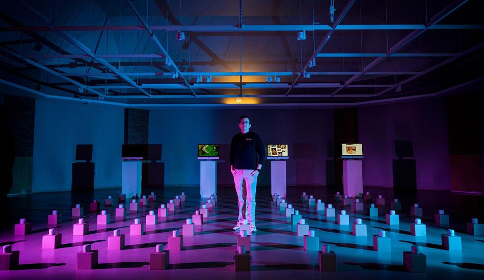 Josh among an art exhibit of many tea cups on boxes laid out in a grid pattern across the floor.