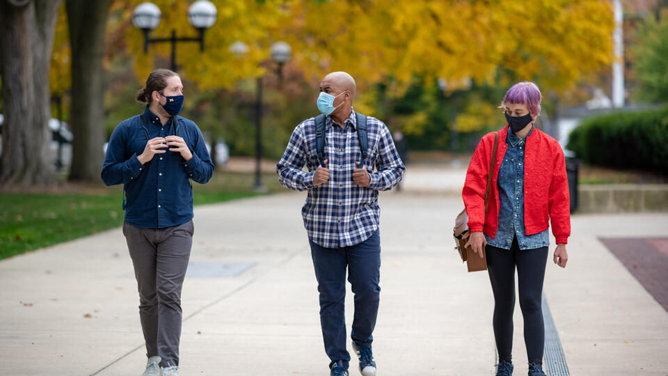 Three students walking on the University of Michigan campus and wearing masks