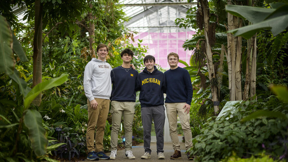 Four students wearing U-M sweatshirts stand in the indoor conservatory at Matthaei Botanical Gardens.