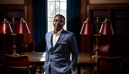 Joel Adu Brimpong standing in front of a large dark wooden table.