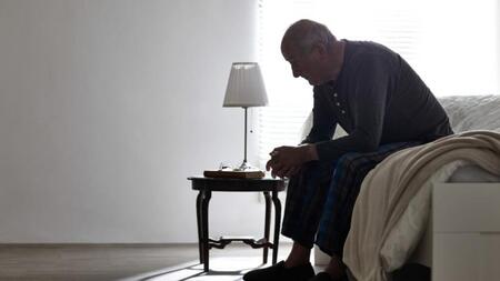 Elderly man sitting on edge of bed