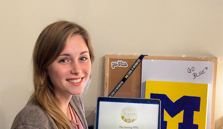Syndey Vollmar sitting at a desk with Michigan swag and a laptop open the The Setting's website