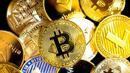 Image shows a loose pile of gold coins representing assorted cryptocurrencies, including Bitcoin, Ethereum and Litecoin. 