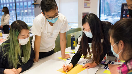 Four students standing around a table and writing with markers