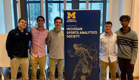The Michigan Sports Analytics Society leadership board poses with a banner that reads “School of Information welcomes Michigan Sports Analytics Society” at the Michigan Sports Analytics Symposium, March 30, 2022 in North Quad Space 2435. 