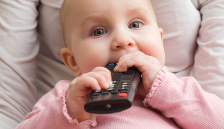 Baby wearing a long-sleeve pink shirt and holding a remote to their mouth.