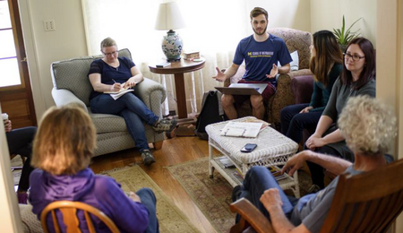 A group of students and community members talking in a living room.
