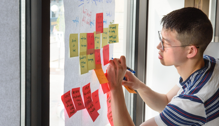 A student writing on a stickie note on a wall covered in other stickie notes