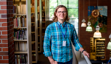 A student standing on the second floor of the Ann Arbor District Library. He is standing next to bookshelves on one side and a balcony on the other.