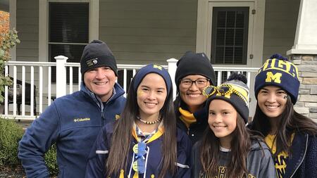 Mike and Lisa Burke with their three daughters dressed in University of Michigan apparel, standing outside. 