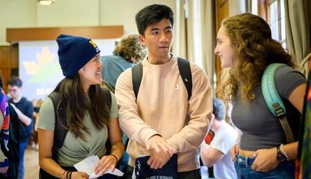 Three students talk in a large conference room.