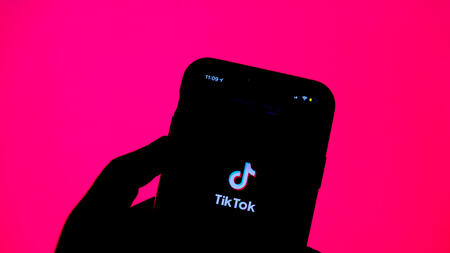 A hand holds a cell phone with the TikTok logo displayed. 