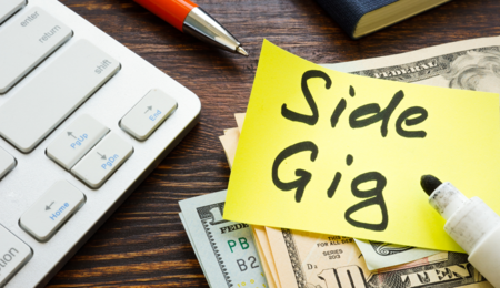 A photo of a keyboard, $10 bills, a pen and a book with a sticky note that says "side gig" in marker.
