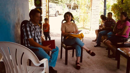 Sylvia in Honduras sitting in a plastic chair talking with residents. 
