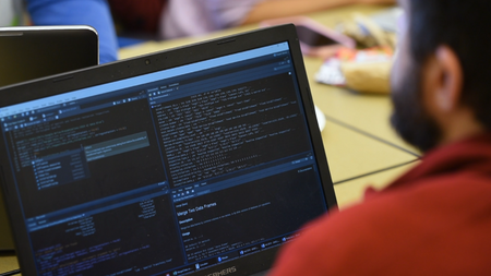 A person looking at a laptop screen. There are four different windows open on the screen and they have code on them.