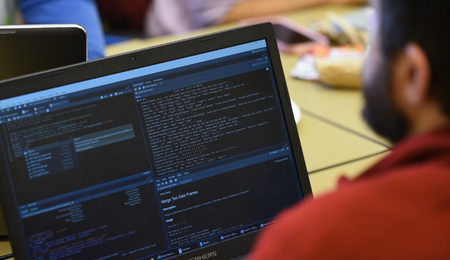 A person looking at a laptop screen. There are four different windows open on the screen and they have code on them.